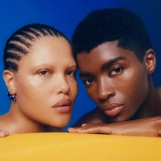 A man and a women behind a yellow table resting their heads on their hand in front of a blue background