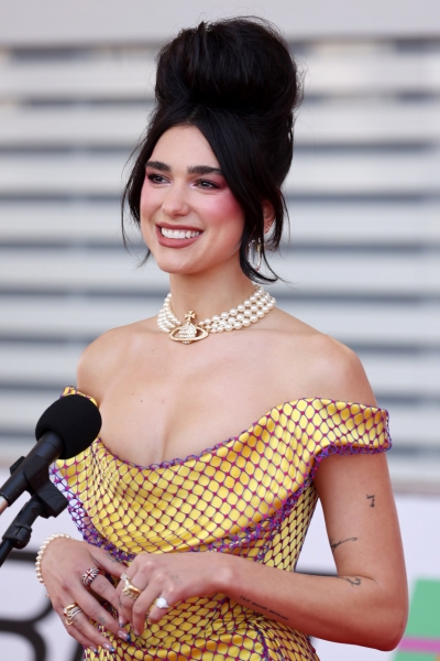 Dua Lipa wearing the modern beehive hair trend on the 2021 BRIT Awards red carpet in a yellow and purple fishnet dress